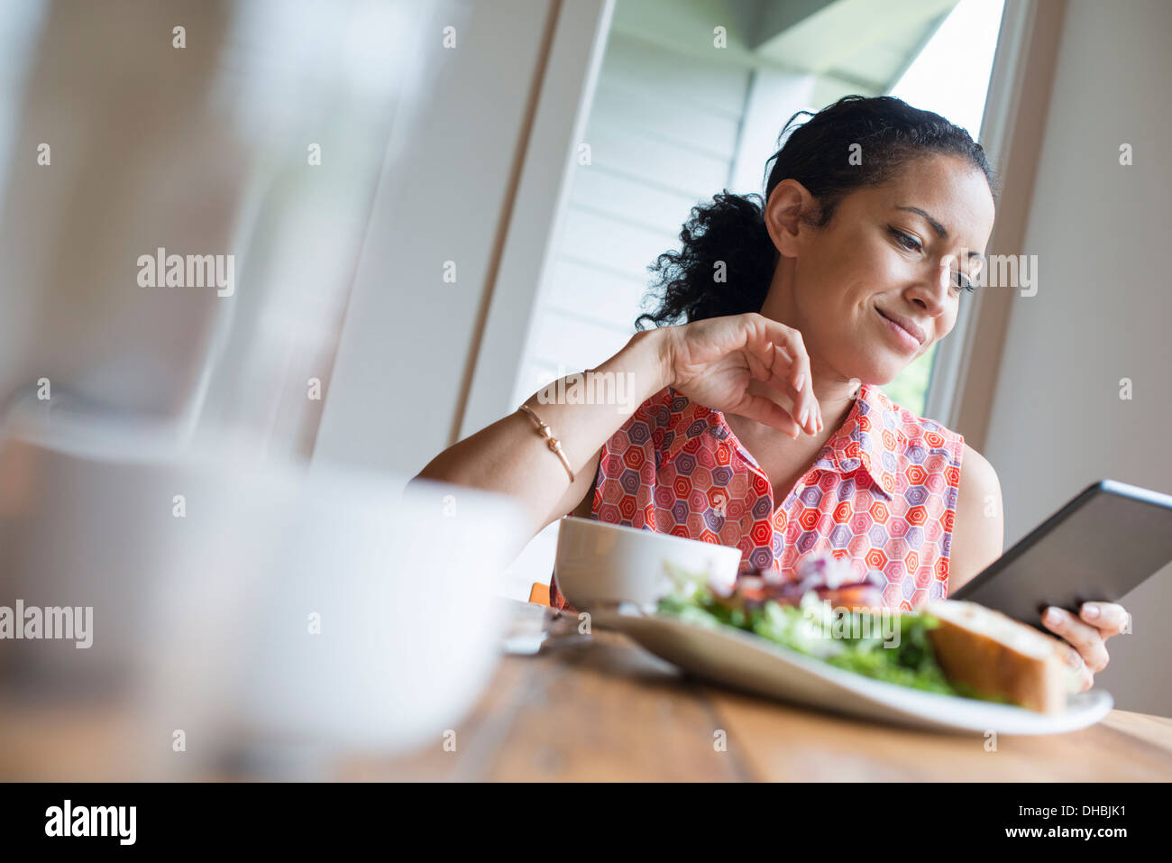 Eine junge Frau, lesen vom Bildschirm des digital-Tablette, an einem Tisch sitzen. Kaffee und ein Sandwich. Stockfoto