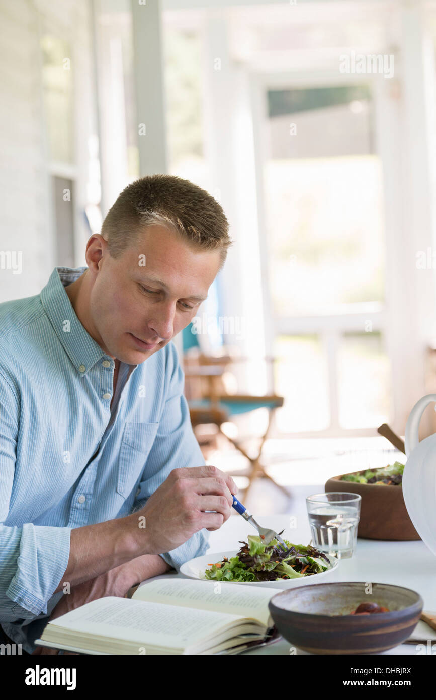 Ein Mann sitzt an einem Cafétisch Essen einen Salat und ein Buch zu lesen. Stockfoto