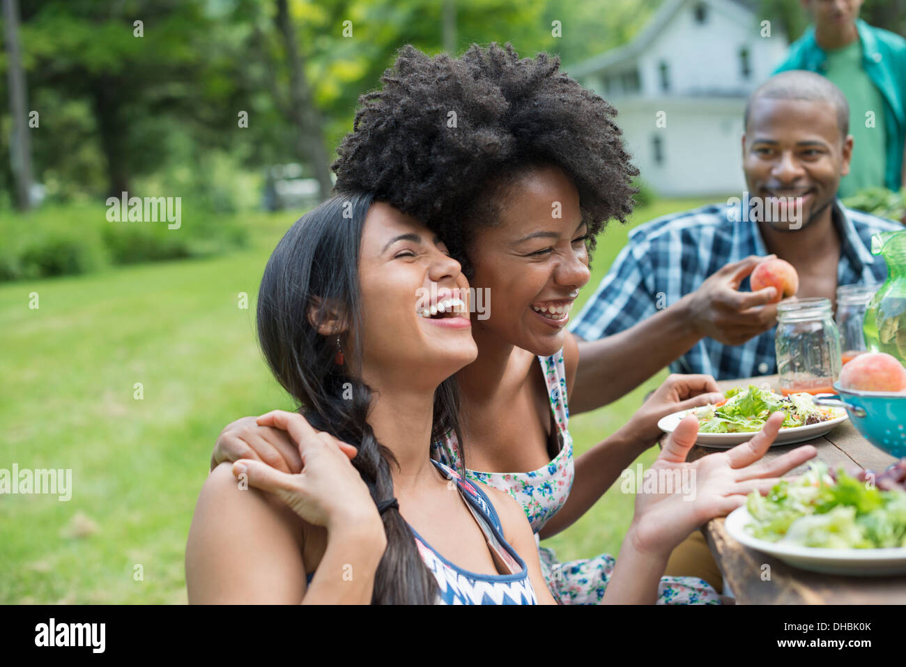 Eine Gruppe von Erwachsenen und Jugendlichen bei einer Mahlzeit im Garten eines Bauernhauses. Vorbei Teller und Gläser erhöhen. Stockfoto