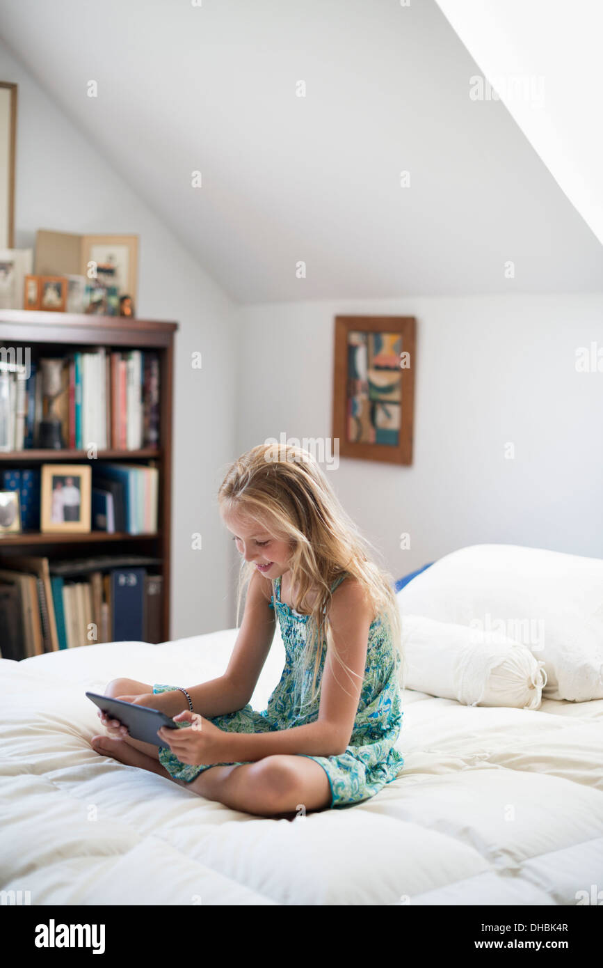 Ein junges Mädchen sitzt auf ihrem Bett mit einem digitalen Tablet. Stockfoto
