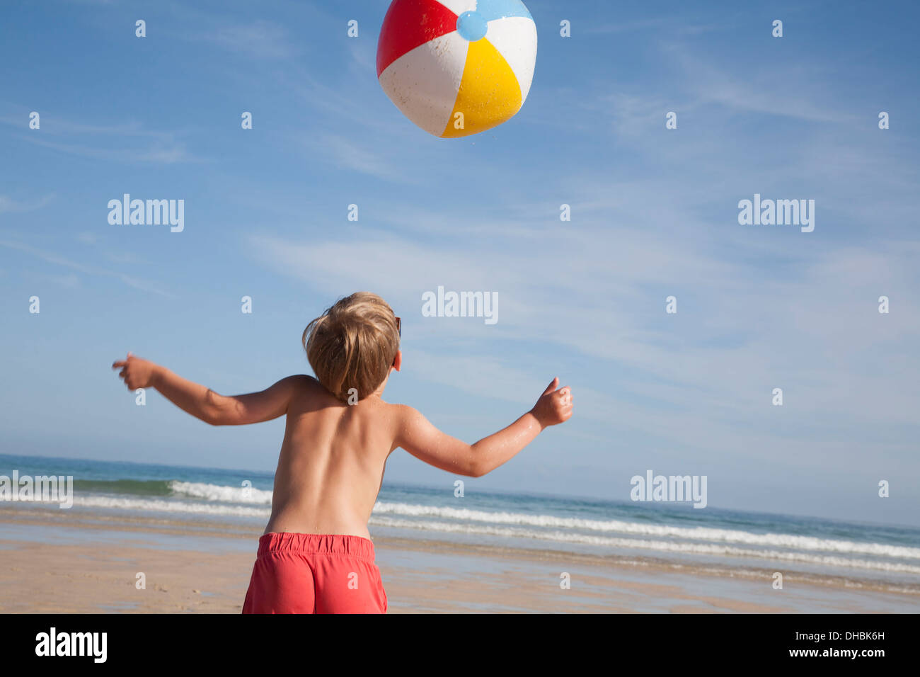 Ein Junge in der Badehose am Strand, mit einer großen Beach-Ball in der Luft über ihn. Stockfoto