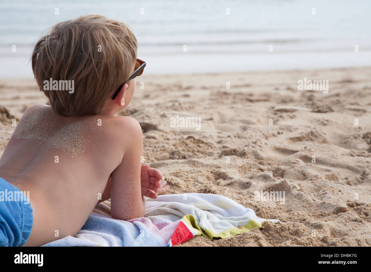 Ein Junge, der auf seiner Vorderseite auf dem Sand, Blick auf das Meer liegen. Stockfoto