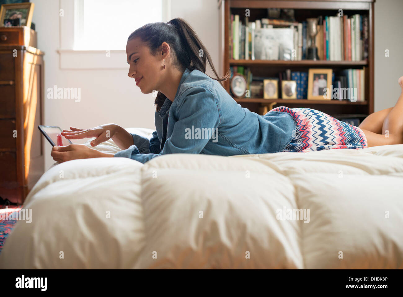 Eine junge Frau liegt auf ihrem Bett mit einem digitalen Tablet. Stockfoto