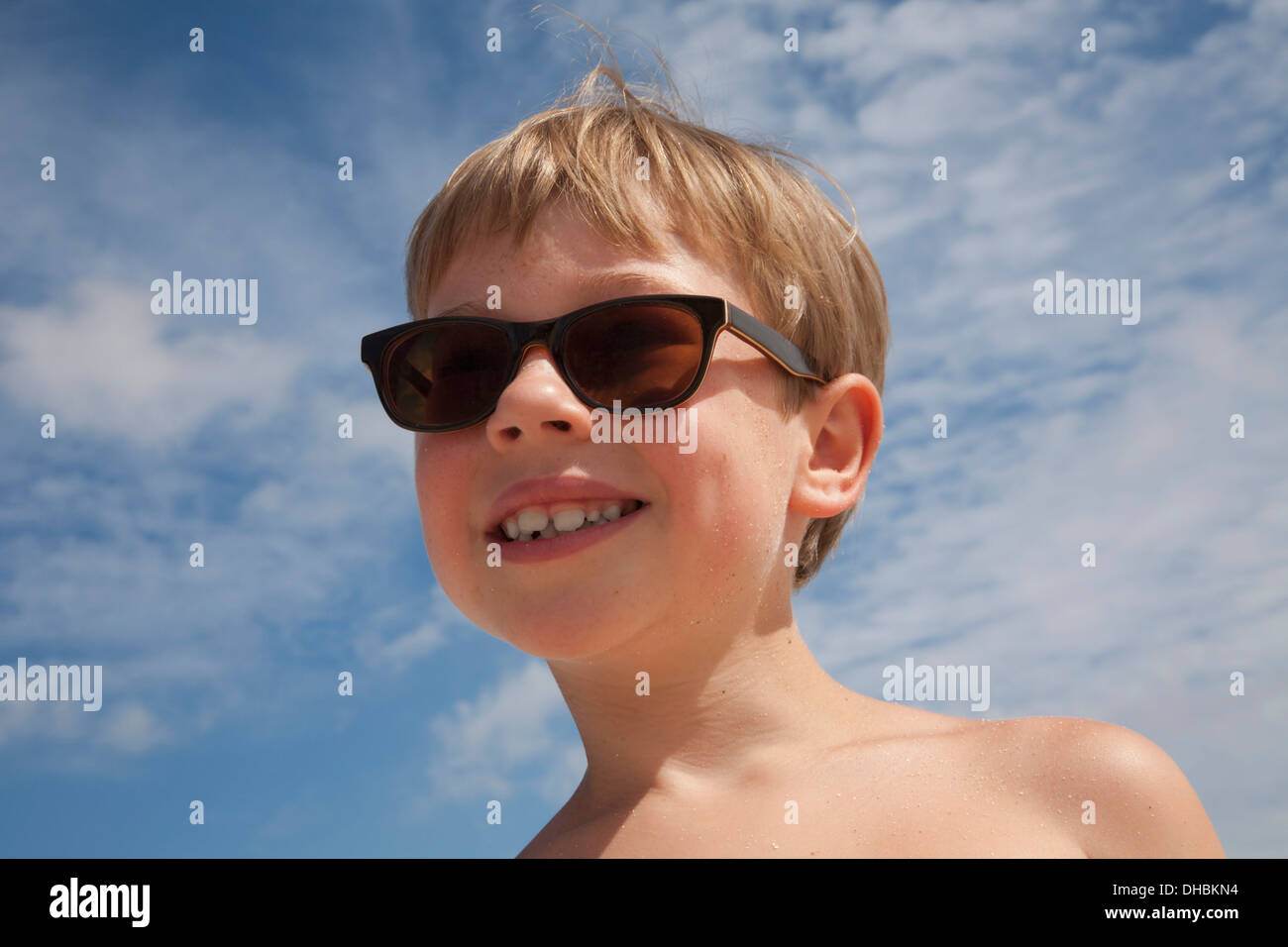 Ein kleiner Junge mit Sonnenbrille. Lächelnd, blauer Himmel. Blonde Haare. Stockfoto