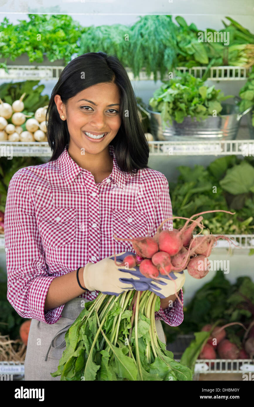 Eine Farm mit Reihen von frisch geerntetem Gemüse zum Verkauf stehen. Eine Frau hält eine Reihe von Karotten. Stockfoto