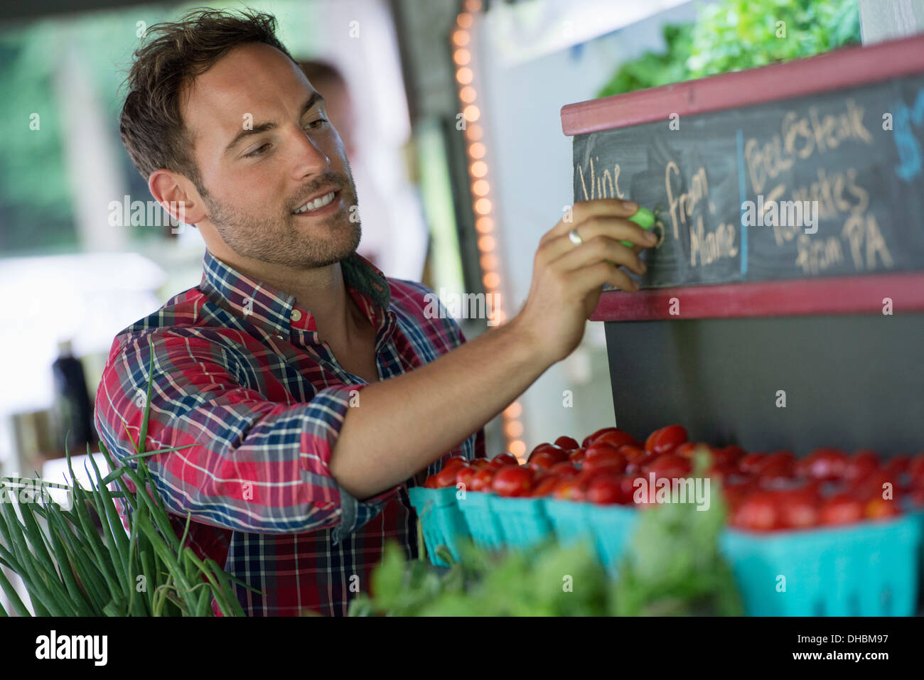 Ein Bio-Obst-Stand. Ein Mann, Kreiden, die Preise an die Tafel. Stockfoto