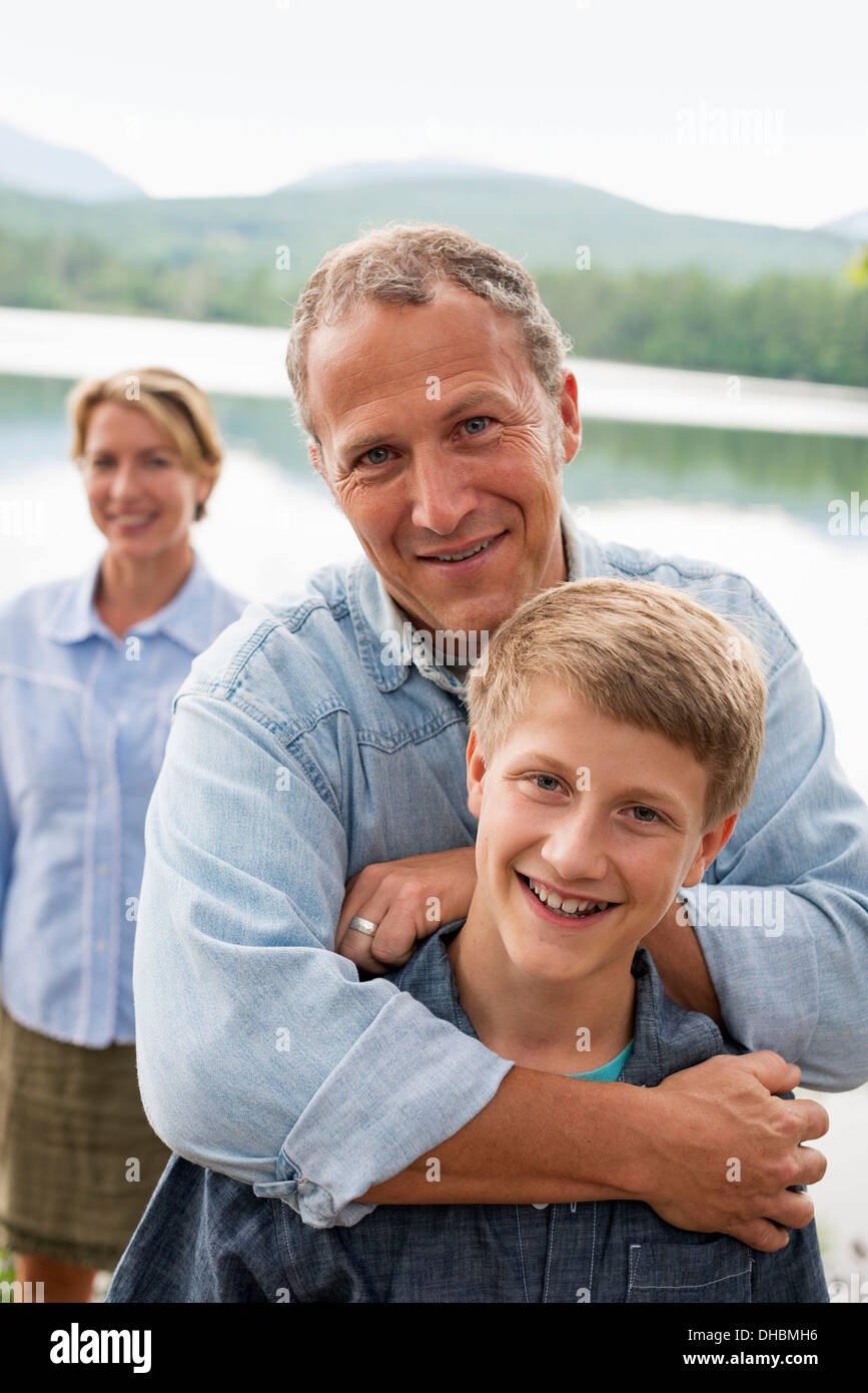 Eine Familie im Freien unter den Bäumen am Ufer eines Sees. Zwei Erwachsene und ein kleiner Junge. Stockfoto