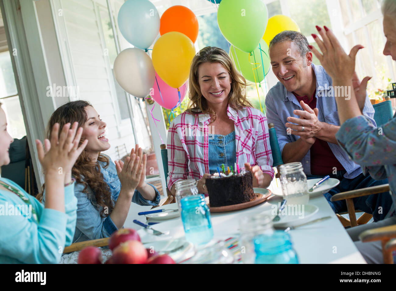 Eine Geburtstagsfeier in einer Landhausküche. Eine Gruppe von Erwachsenen und Kinder versammelten sich um einen Schokoladenkuchen. Stockfoto