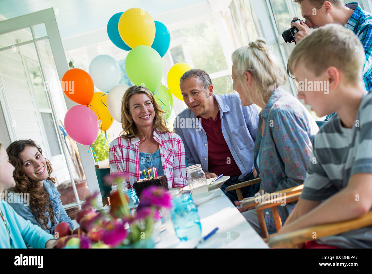 Eine Geburtstagsfeier in einer Landhausküche. Eine Gruppe von Erwachsenen und Kinder versammelten sich um einen Schokoladenkuchen. Stockfoto