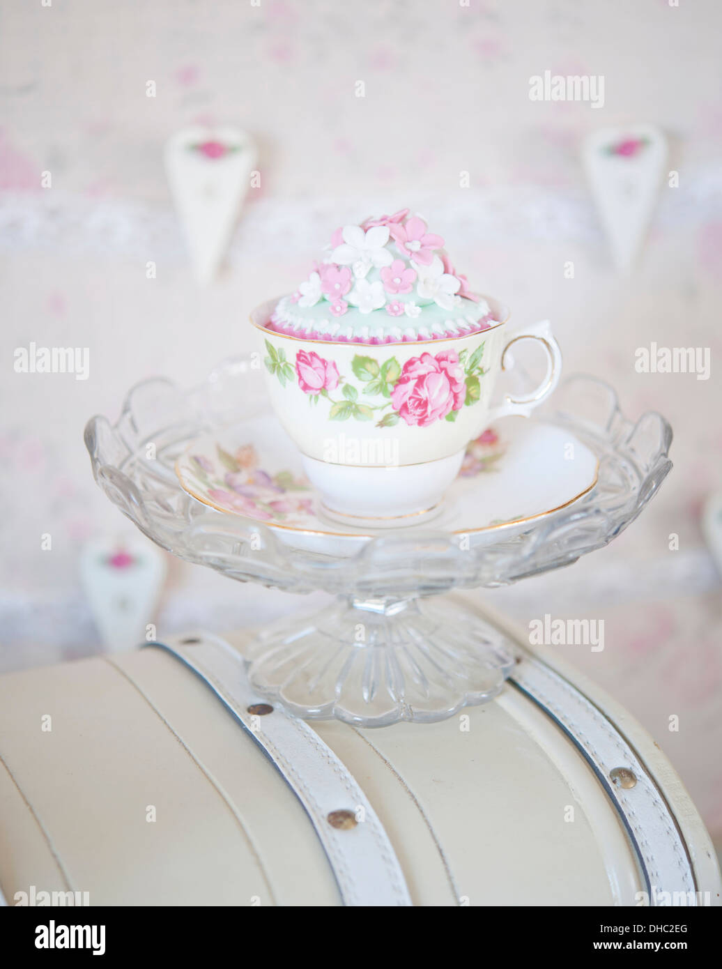 Eine florale China Tasse und Untertasse mit Cupcake, ruht auf einer Glasschale Stockfoto