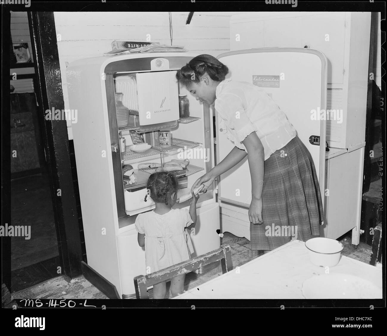 Mrs. James Robert Howard versorgt ihre Tochter mit einer Banane aus dem elektrischen Kühlschrank, die die Rolle der Elektrizität für den Komfort im Haushalt während des frühen 20. Jahrhunderts demonstriert. Stockfoto