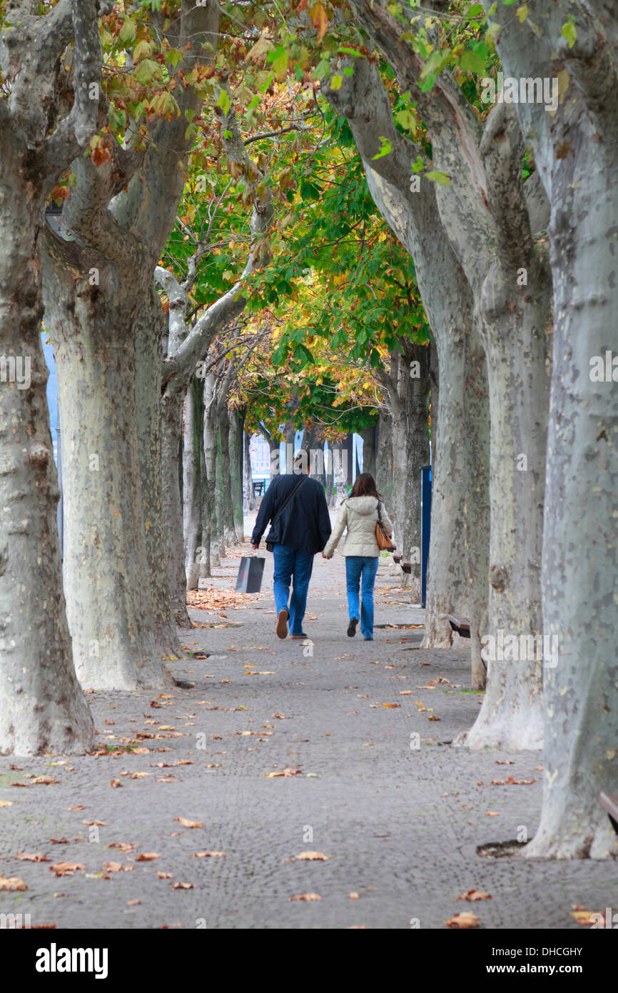 Ein paar zu Fuß entlang des Baums gesäumten Promenade am Comer See in Lecco, Italien im Herbst. Stockfoto