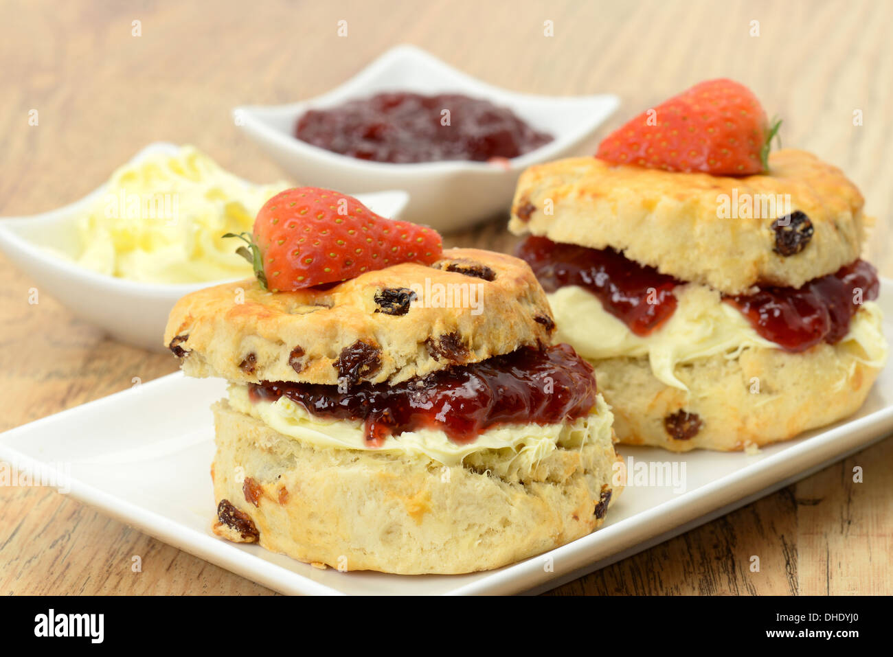 Zwei Creme Tee Scones mit Clotted Cream und Erdbeermarmelade mit Beilagen extra Marmelade und Clotted Cream - Studio gedreht Stockfoto