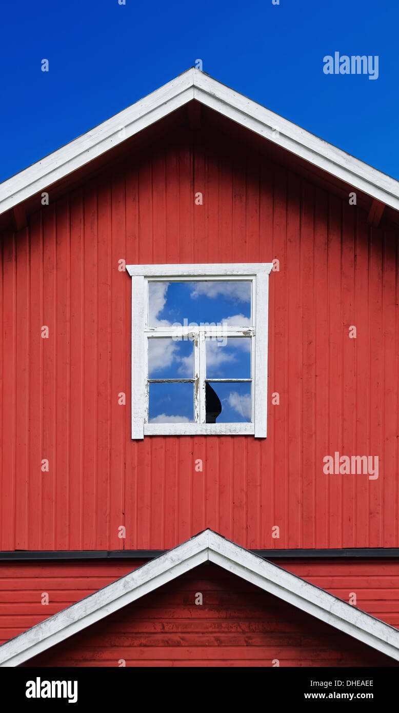 Zerbrochenes Fenster eines alten roten hölzernen Gebäudes. Blauer Himmel und Wolken Reflexionen. Stockfoto