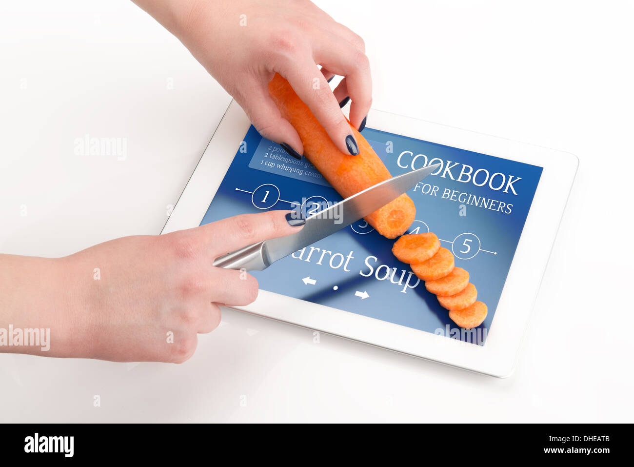Frauenhände schneidet der Karotte auf einem Tablet PC, auf dem gibt es eine Rezept Karottensuppe. Stockfoto