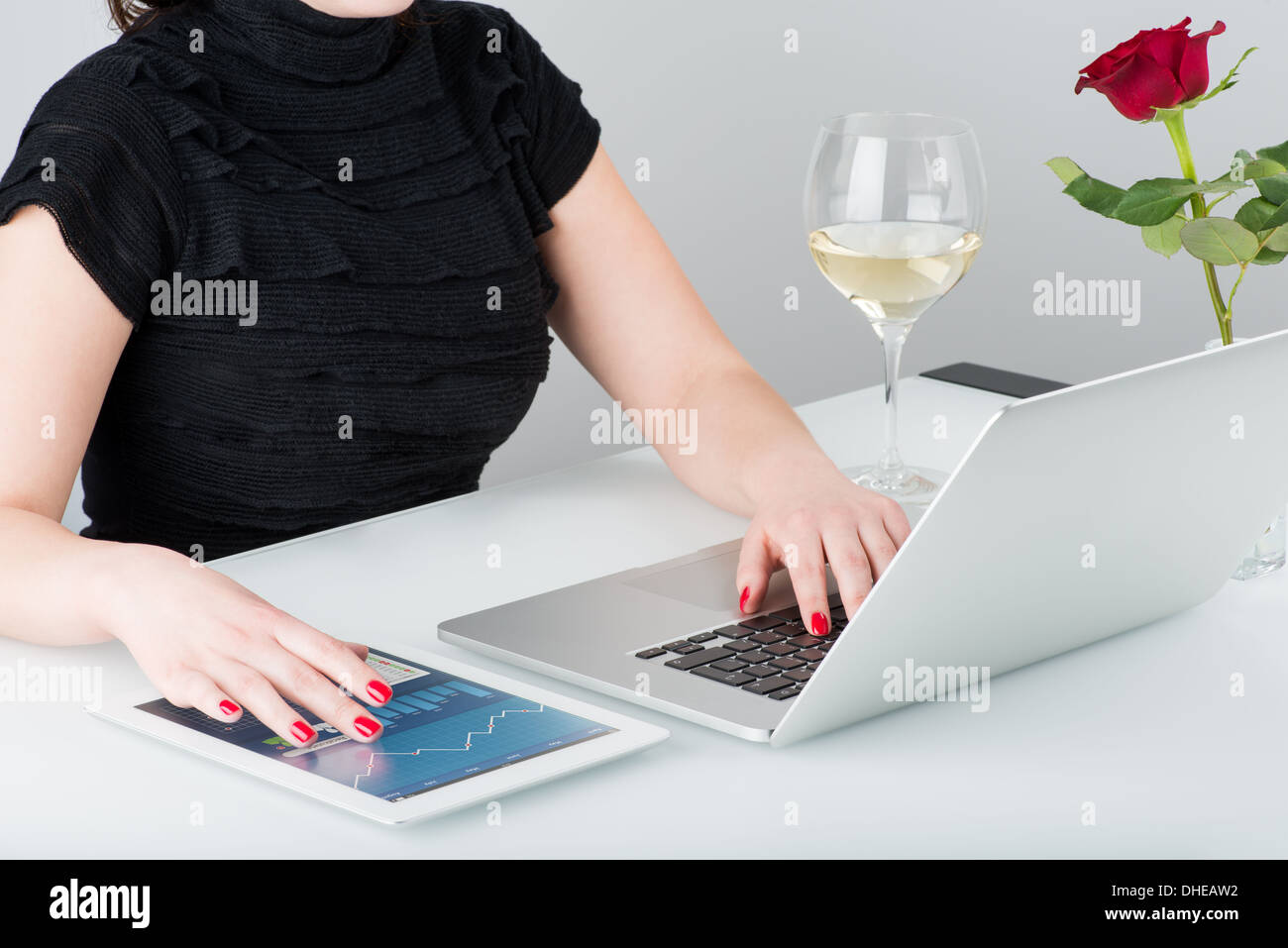 Eine Geschäftsfrau arbeitet mit modernen Laptop und Tablet-Computer. In der Nähe auf der Tisch ist ein Glas Wein und eine Rose. Stockfoto