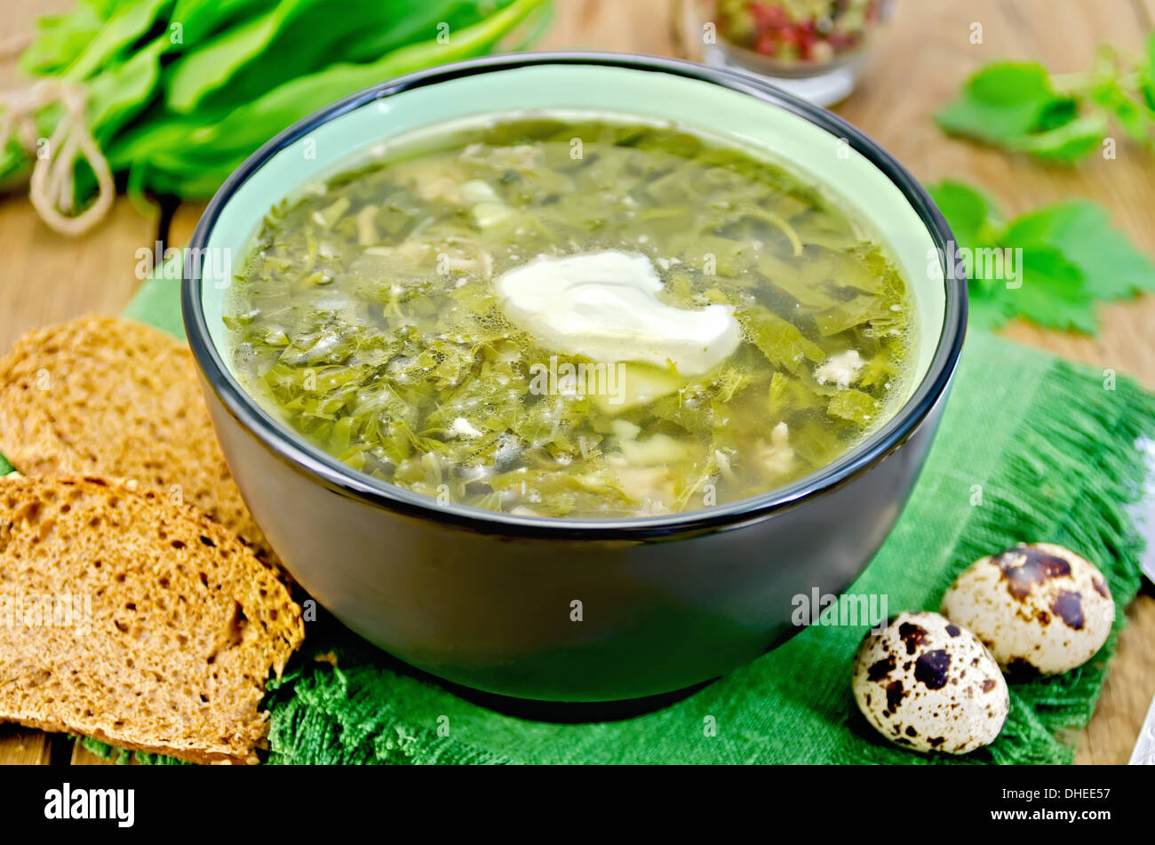 Grüne Suppe von Ampfer, Brennnessel und Spinat in eine Schüssel geben, Wachteleier, Brot, Pfeffer gegen ein Holzbrett Stockfoto