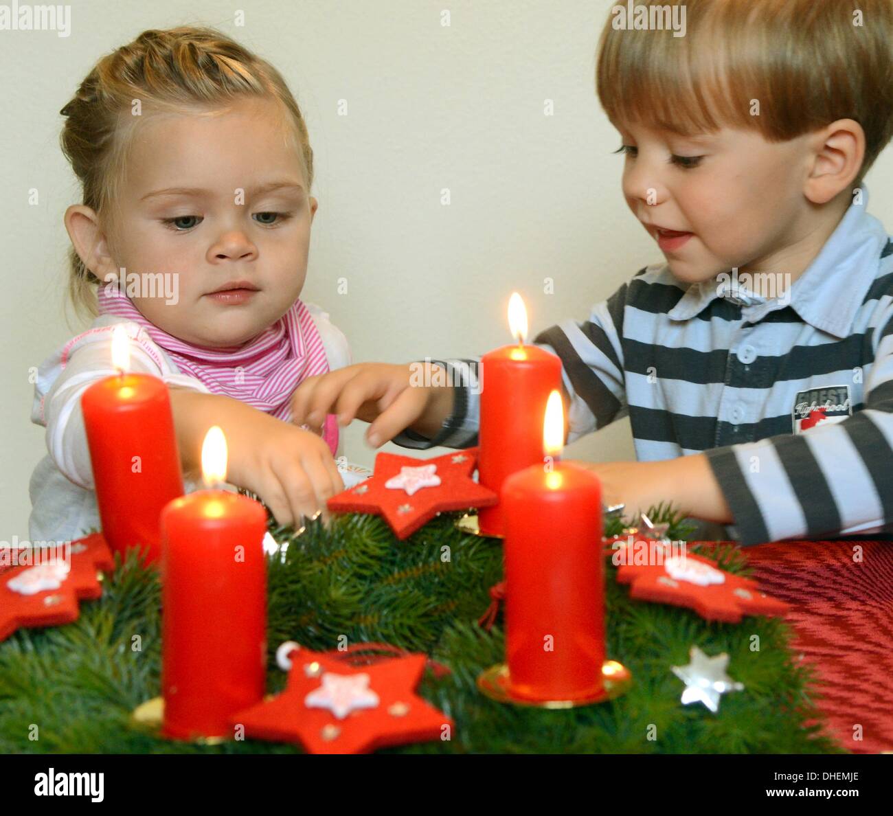 Ein kleines Mädchen und ein kleiner Junge sitzen vor einem Adventskranz mit 4 brennende Kerzen unter der Aufsicht ihrer Eltern am 9. Oktober 2013. Foto: Waltraud Grubitzsch - Model-release Stockfoto