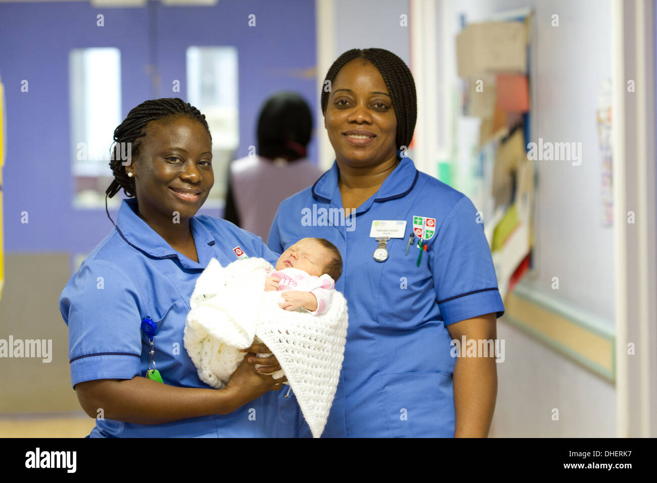Eine Hebamme hält ein neugeborenes Baby, während ein Kollege in einem Krankenhausflur UK steht Stockfoto