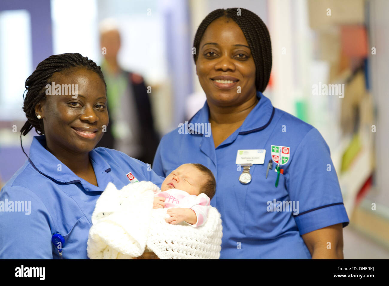 Eine Hebamme hält ein neugeborenes Baby, während ein Kollege in einem Krankenhausflur UK steht Stockfoto