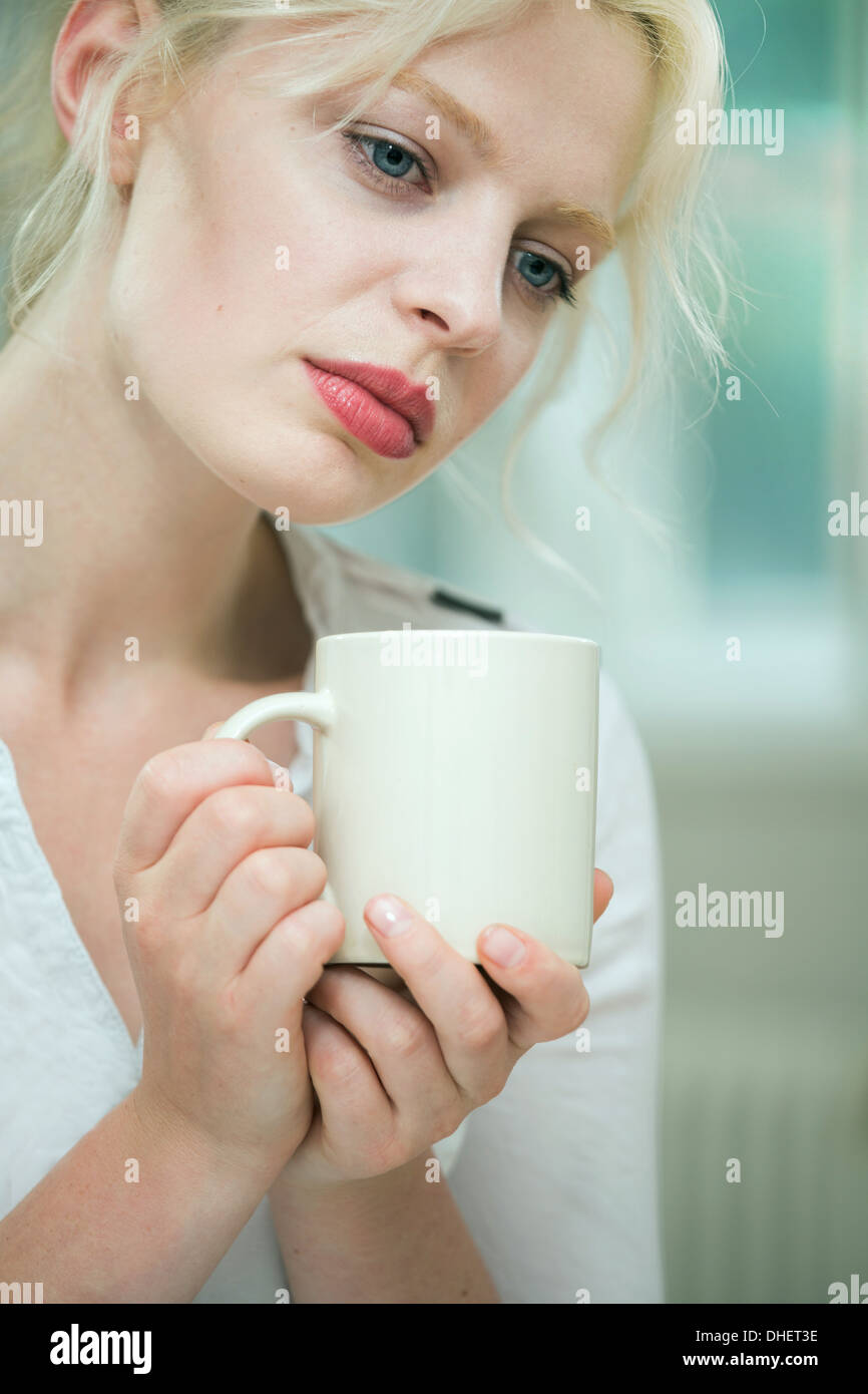 Wehmütig aussehende junge Frau mit einem Kaffee Stockfoto