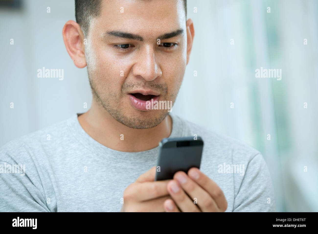 Mitte erwachsenen Mannes auf der Suche nach Smartphone überrascht Stockfoto