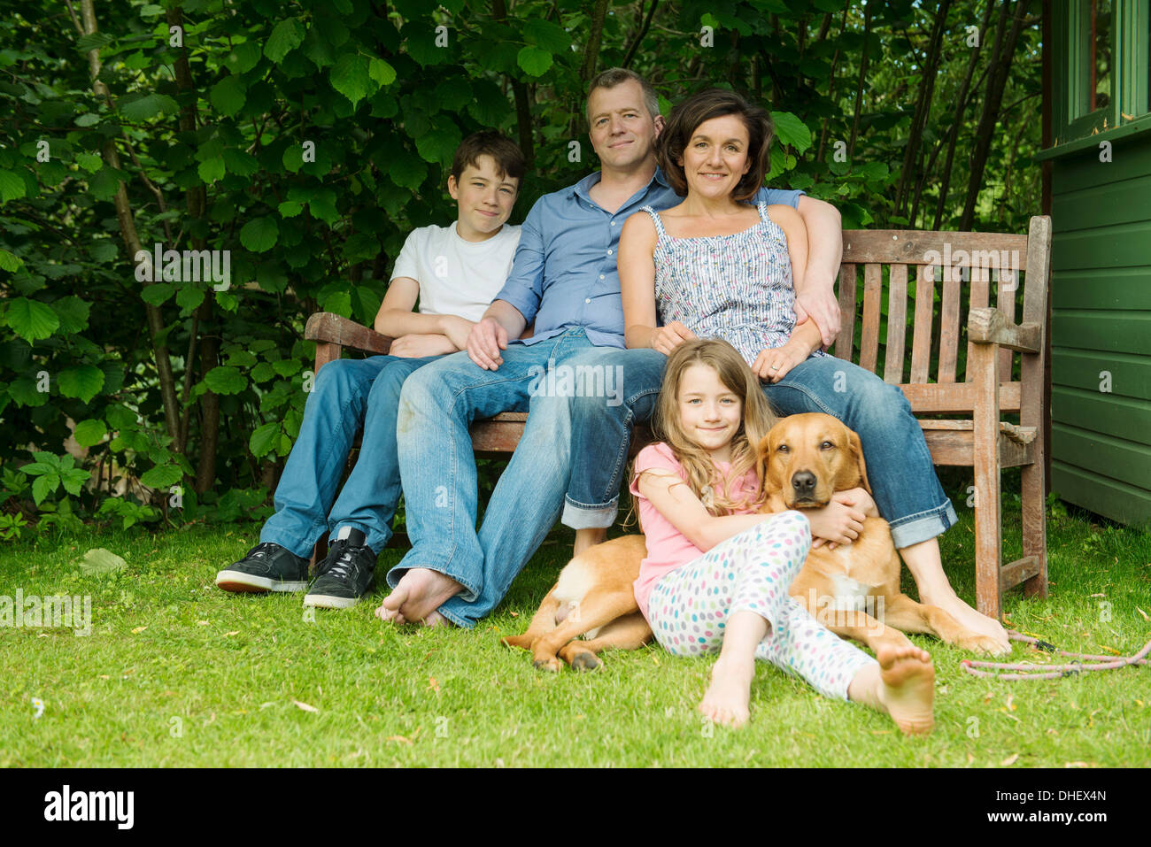 Porträt der Familie mit zwei Kindern sitzen auf Gartenbank mit Hund Stockfoto