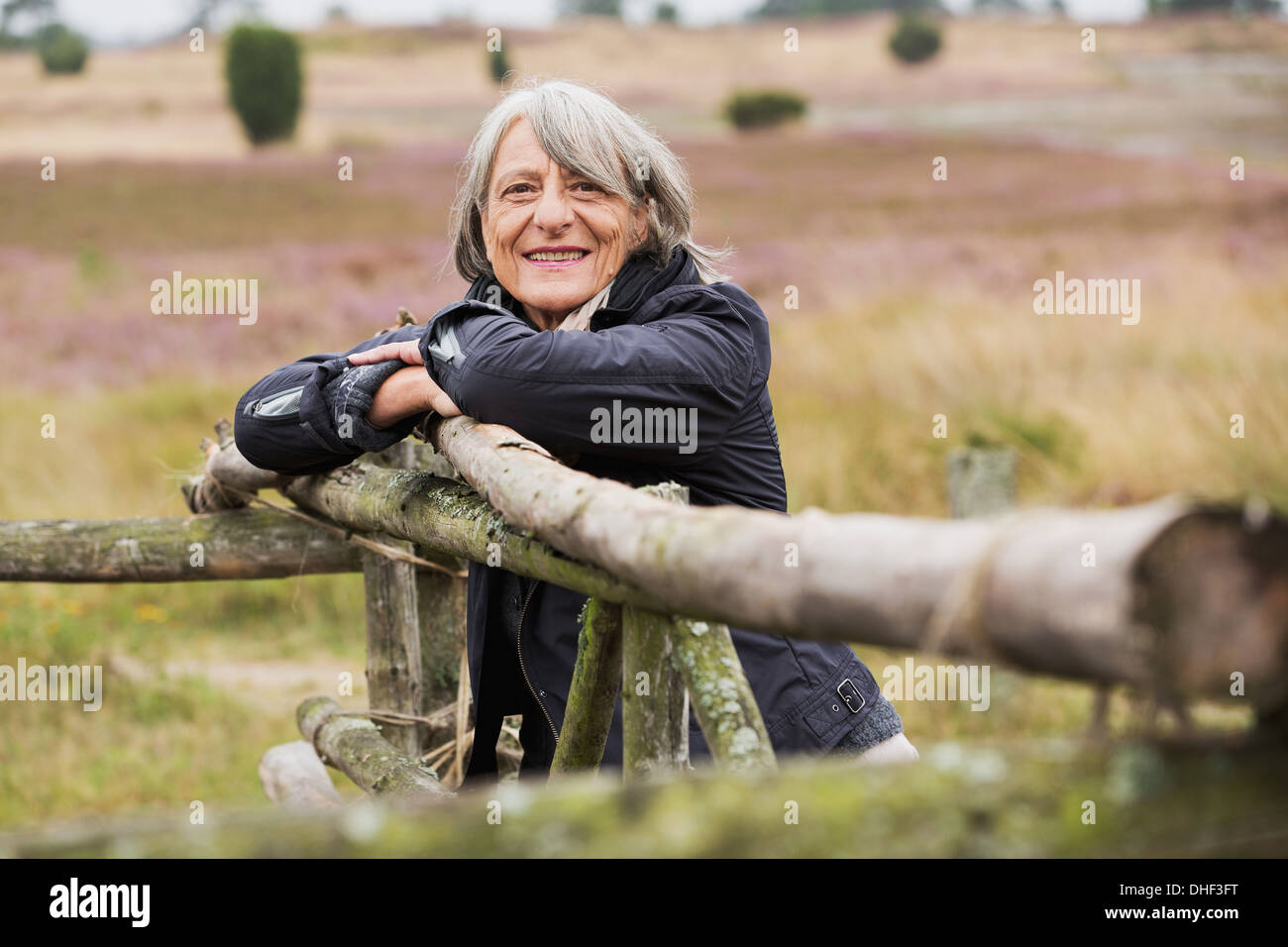 Ältere Frau stützte sich auf Holzzaun lächelnd in Richtung Kamera Stockfoto