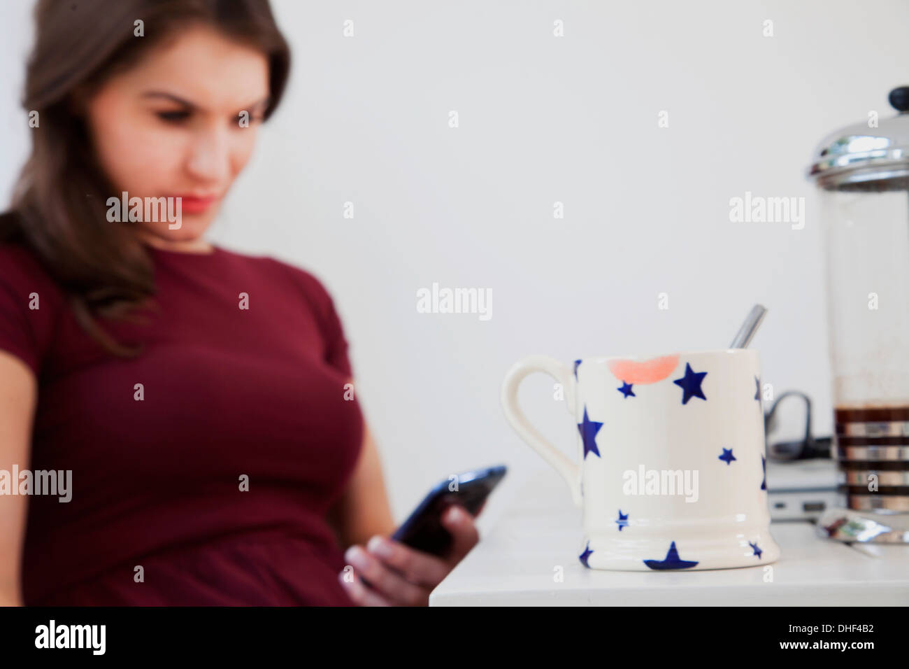 Junge Frau mit Handy mit Kaffeetasse im Vordergrund Stockfoto