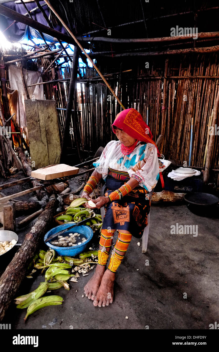 Eine indigene Guna-Frau in traditionellem Gewand schält Bananen in ihrer Küche auf der Insel Carti Sugtupu in der Comarca (Region) der als Kuna bekannten Guna Yala-Ureinwohner, die sich im Archipel der San Blas Blas-Inseln im Nordosten Panamas mit Blick auf das Karibische Meer befindet. Stockfoto