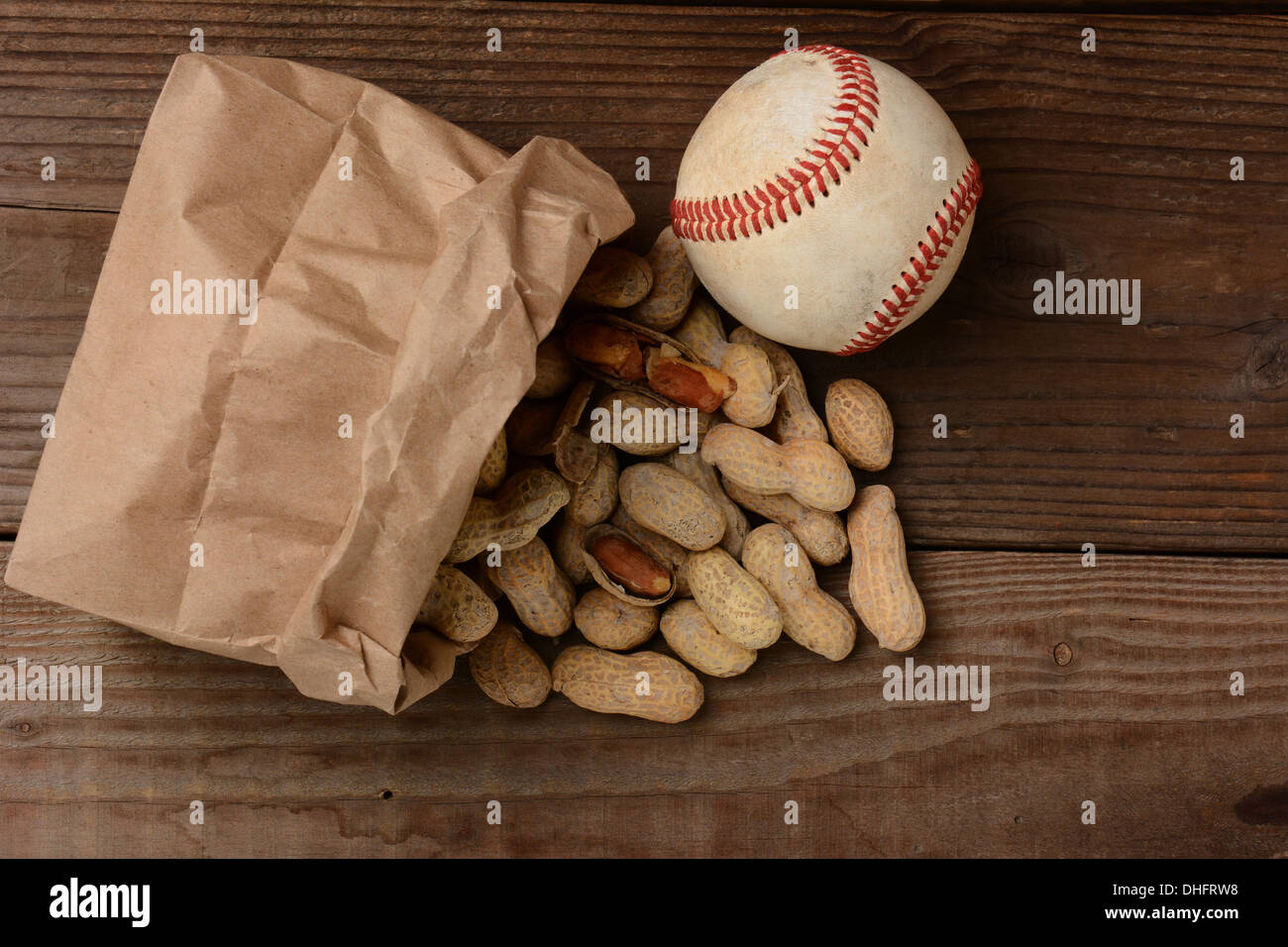 Eine Tasche von Erdnüssen und einen Baseball auf einer alten Holzbank im Stadion. Die Papiertüte ist auf der Seite mit den Muttern verschütten. Stockfoto