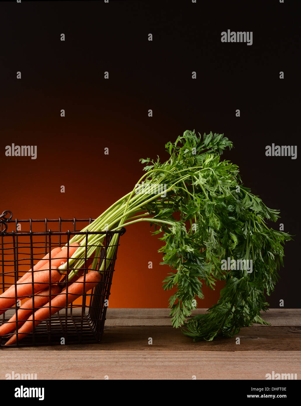 Frisch gepflückt Karotten in einen Drahtkorb mit einem Licht in dunklen warmen Hintergrund. Stockfoto