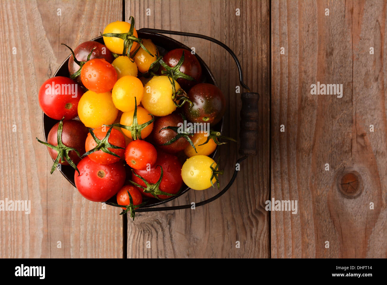 Baby Heirloom Tomatoes in einem Eimer auf einem rustikalen Holztisch. Querformat, schaut auf den Eimer. Stockfoto