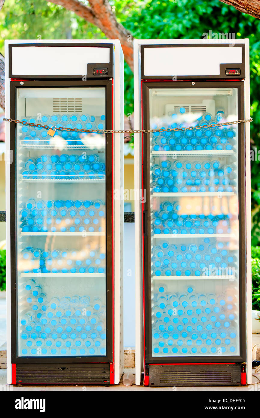 zwei Kühlschränke voller Flaschen mit Wasser hinter Schloss und Riegel Stockfoto