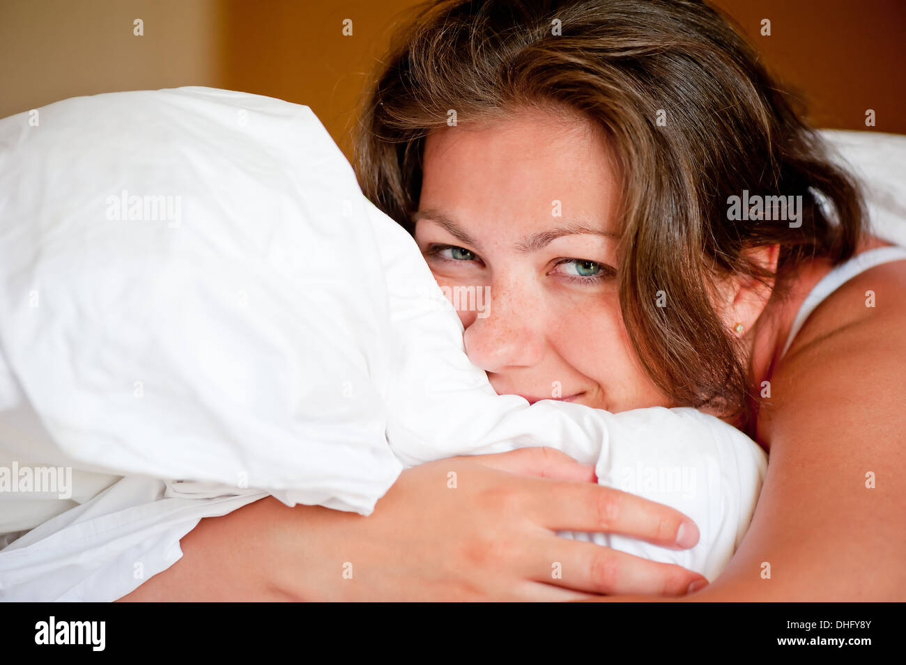 junge Frau umarmt eine Kissen im Bett Stockfoto