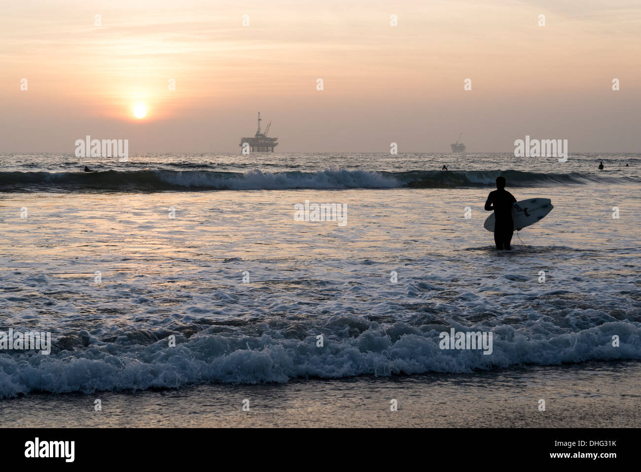 Blick auf ein California Surfer Silhouette gegen die untergehende Sonne, mit einer Offshore-Plattform, die in der Ferne sichtbar. Stockfoto