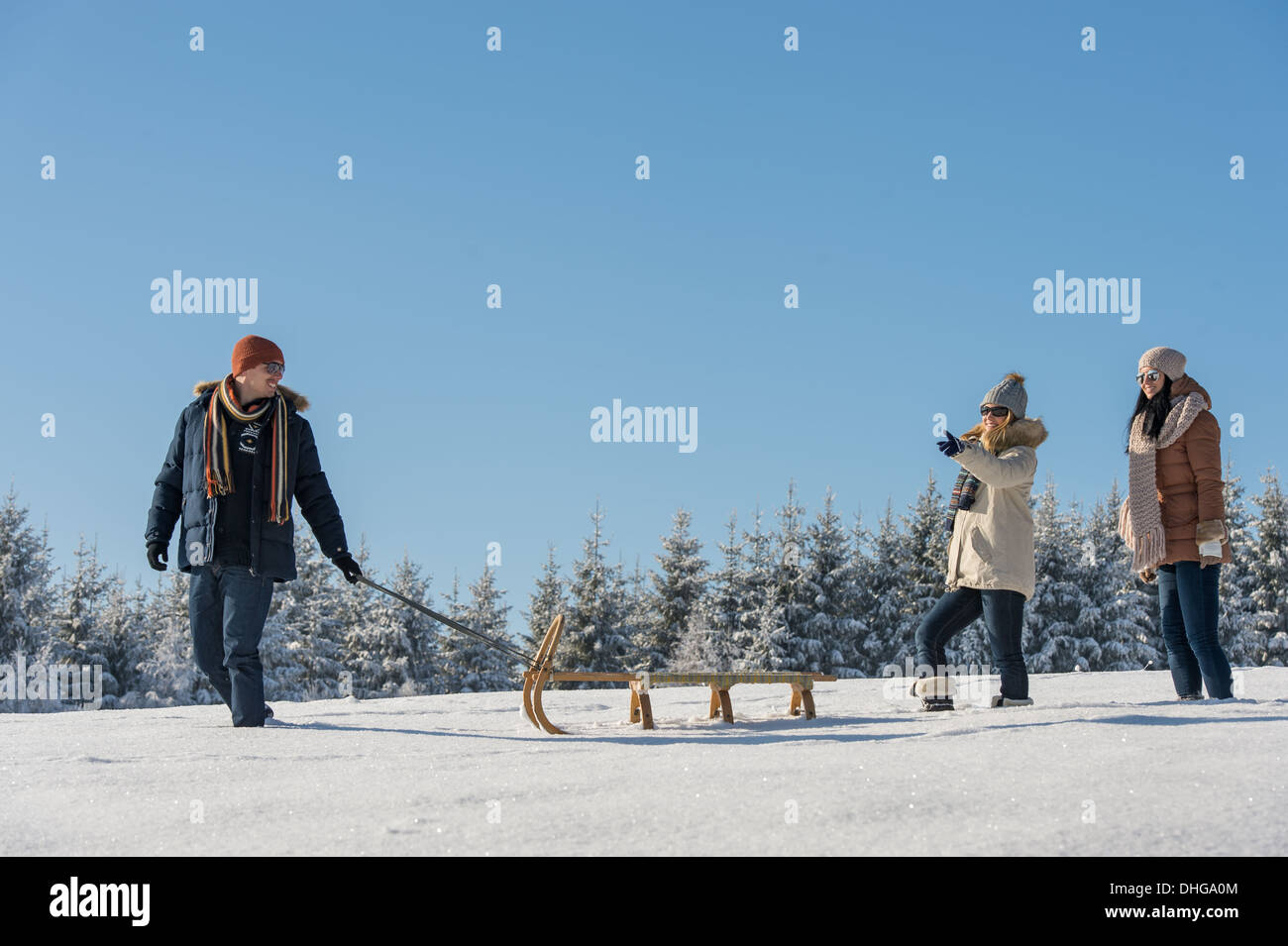 Junger Mann ziehen Schnee Schlitten Winterlandschaft weibliche Freundinnen Stockfoto