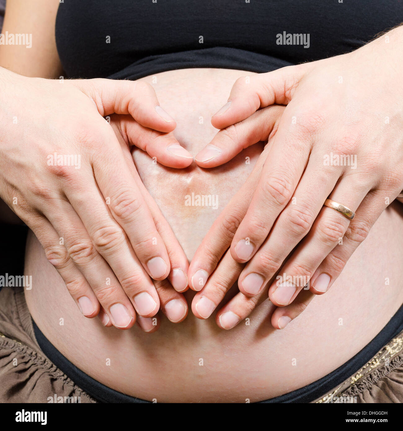 Glückliche Eltern machen Herz mit zwei paar Hände auf Bauch der schwangeren Frau zu unterzeichnen Stockfoto