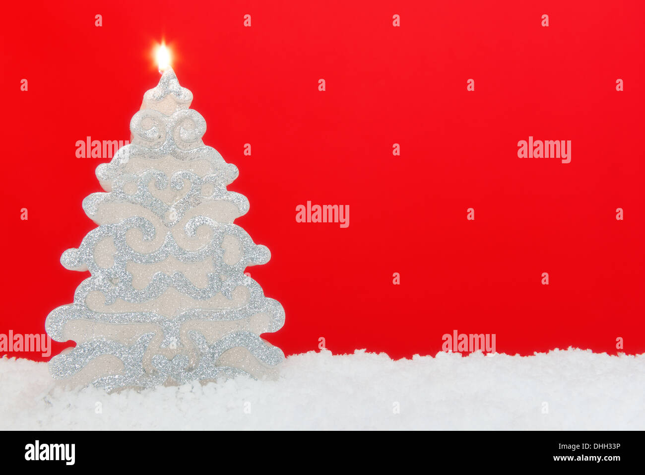 Weihnachtsbaum geformte Kerze auf Schnee vor einem roten Hintergrund. Stockfoto