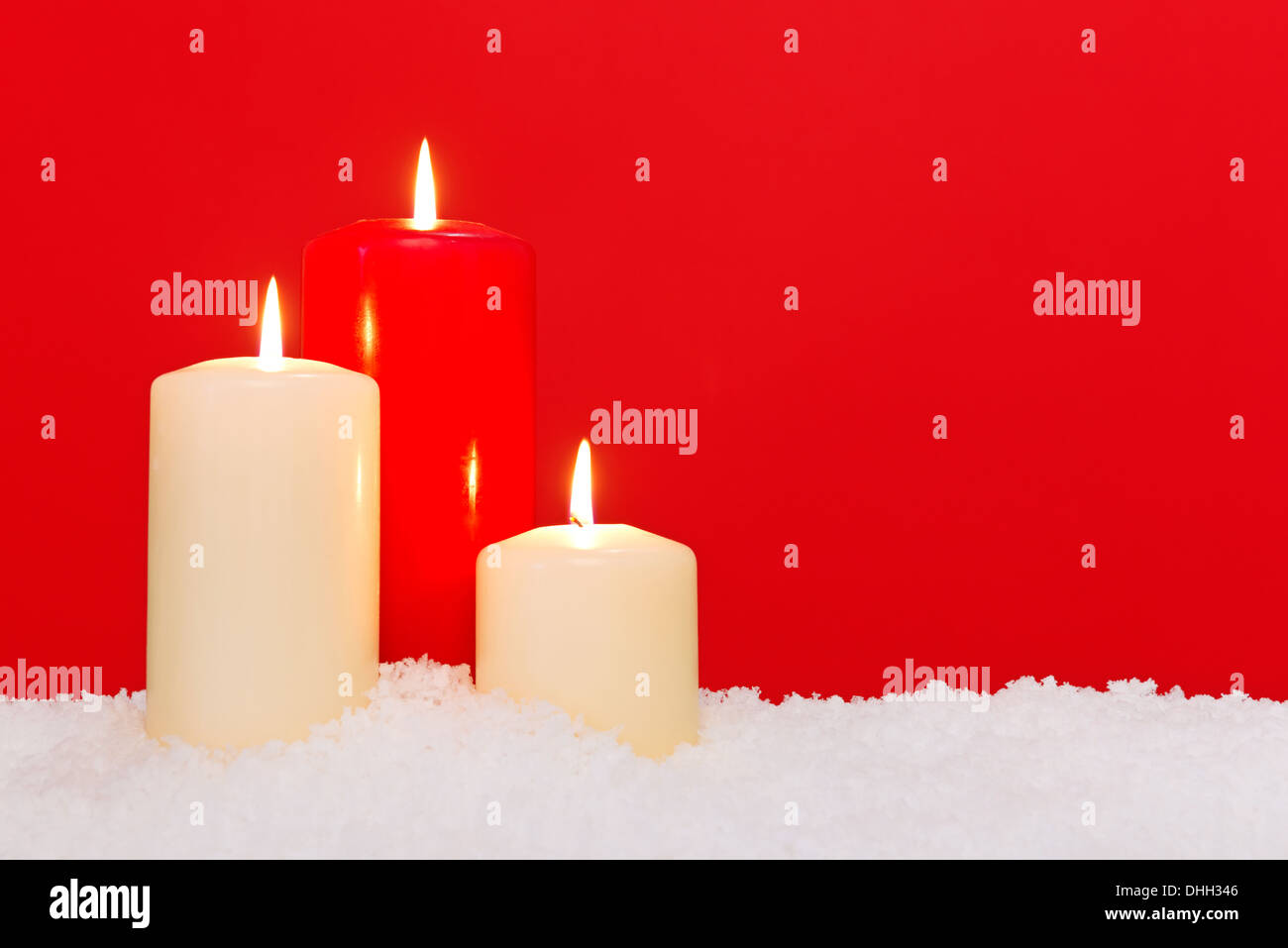 Drei Weihnachtskerzen sitzen im Schnee vor einem roten Hintergrund. Stockfoto