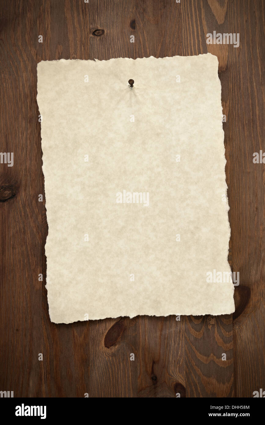 Leeres Pergament-Papier mit zerrissenen Kanten an einer alten Holztür mit einem rostigen Nagel genagelt. Stockfoto