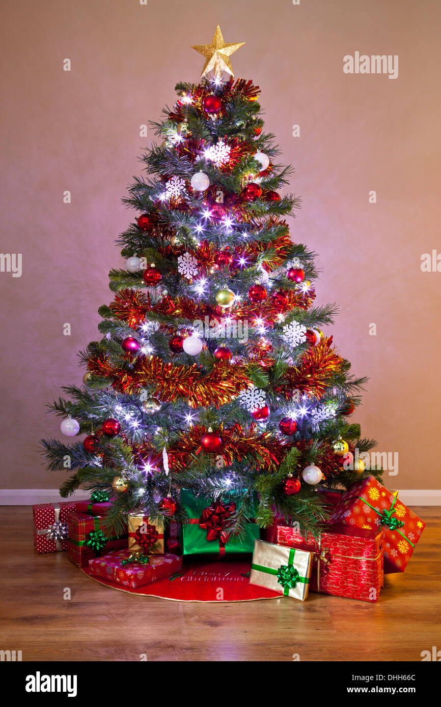 Ein geschmückter Weihnachtsbaum in einem Heim, mit Lichterketten beleuchtet und umgeben von Geschenk verpackt präsentiert. Stockfoto