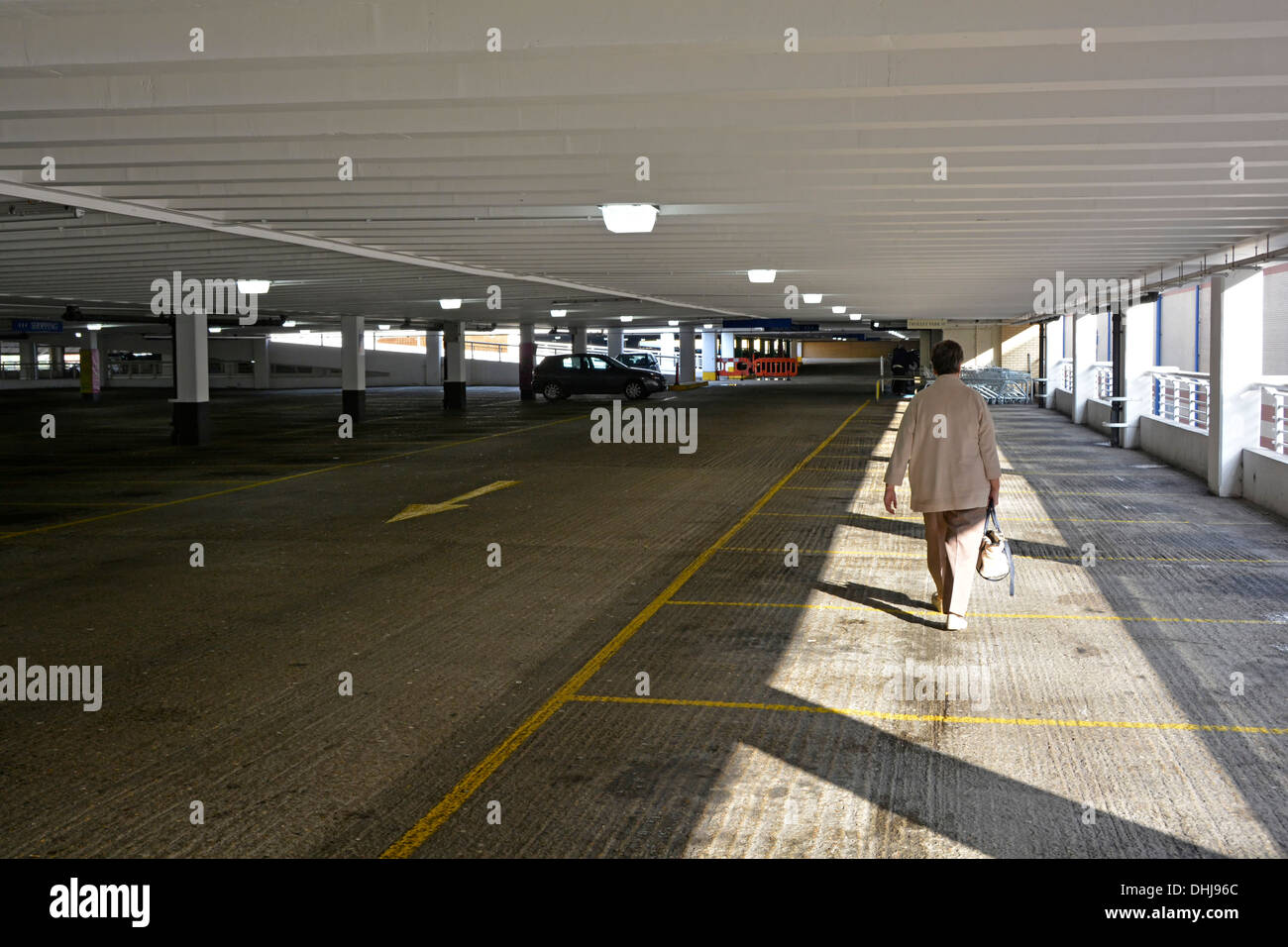 Allein in der Sonne beleuchtete Käuferin, die zum Ausgang geht und Handtasche in einem verlassenen Parkhaus hält Lakeside Einkaufszentrum West Thurrock Essex England Großbritannien Stockfoto