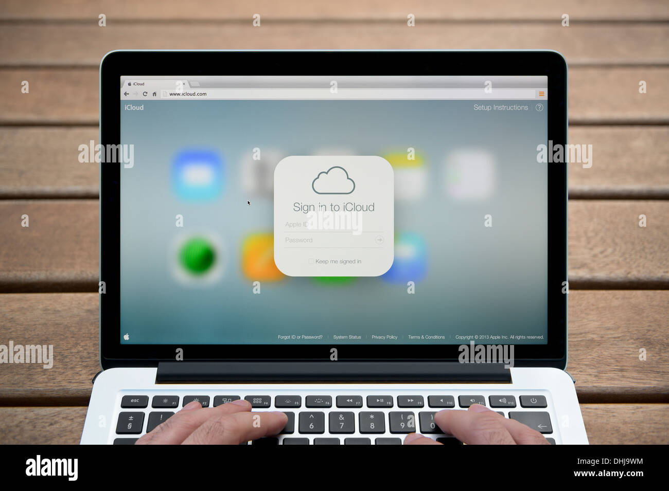 Die iCloud-Logo auf einem MacBook Hintergrund eine Holzbank im Freien einschließlich eines Mannes Finger (nur zur redaktionellen Verwendung). Stockfoto