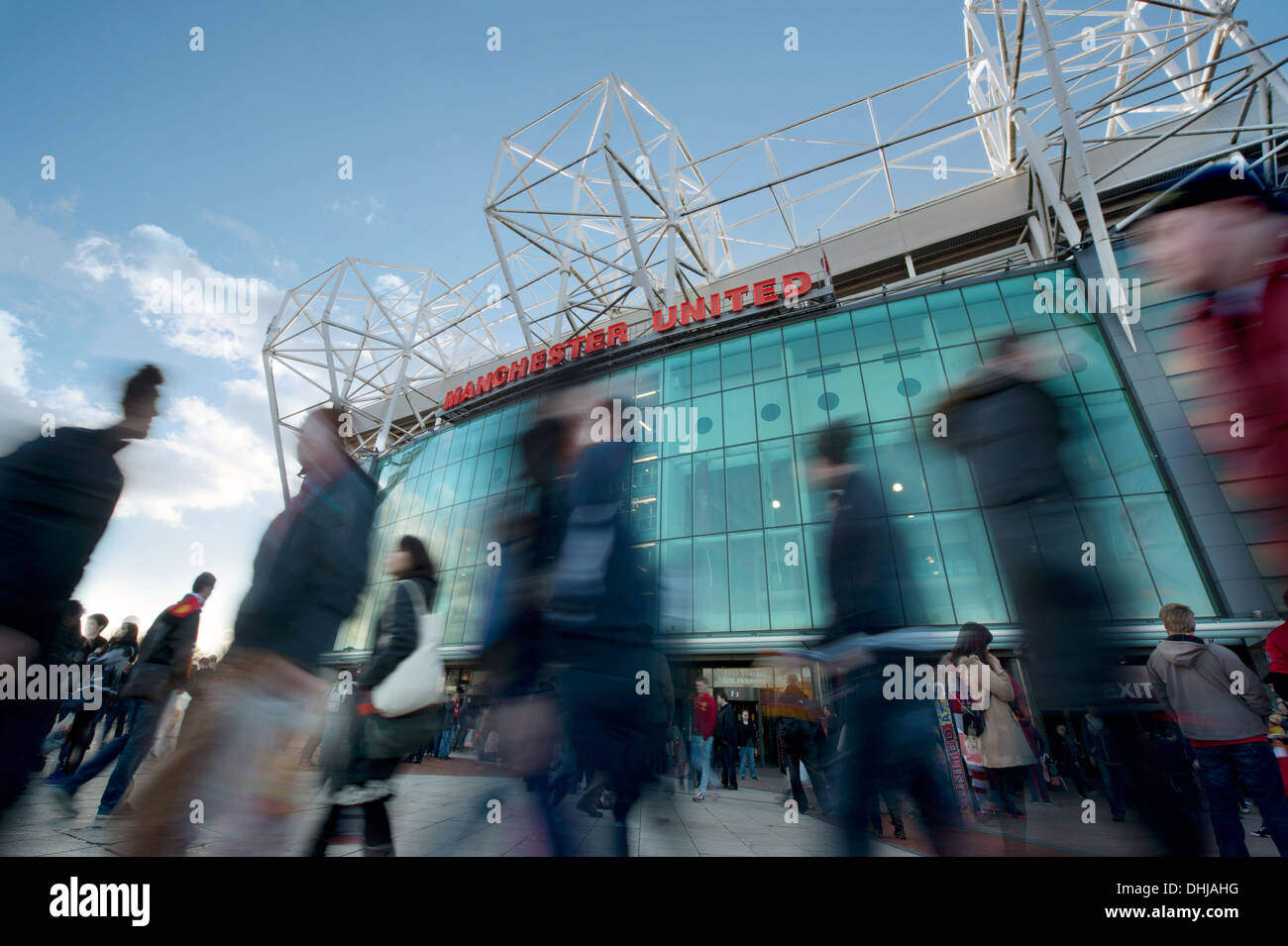 Fans von Manchester United Football Club gehen vorbei an die große Glasfront des Vereins Old Trafford Stadion (nur zur redaktionellen Verwendung). Stockfoto