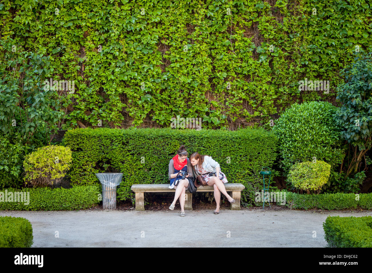 Zwei Touristen-Mädchen, die Fotos auf einer Bank im Hotel de Sully, les Marais, Paris, Frankreich, überprüfen Stockfoto