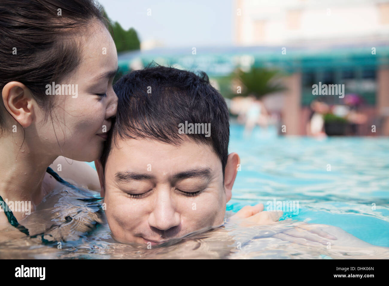 Frau mit Augen geschlossen küssen Mann auf die Wange in das Wasser im pool Stockfoto