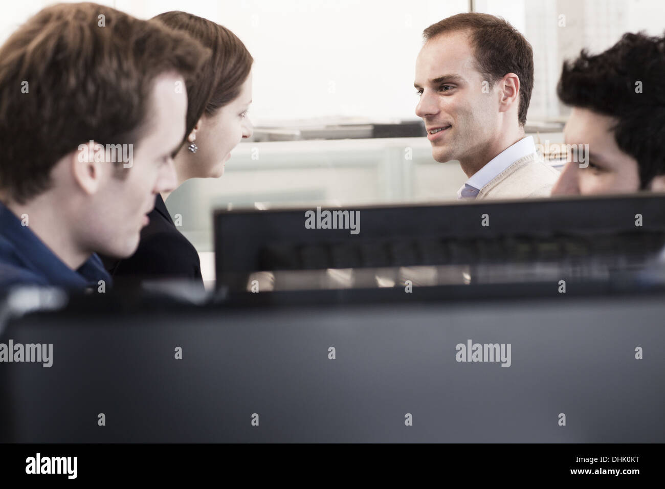 Vier Mitarbeiter sitzen und diskutieren im Büro durch die Computer-Monitore Stockfoto