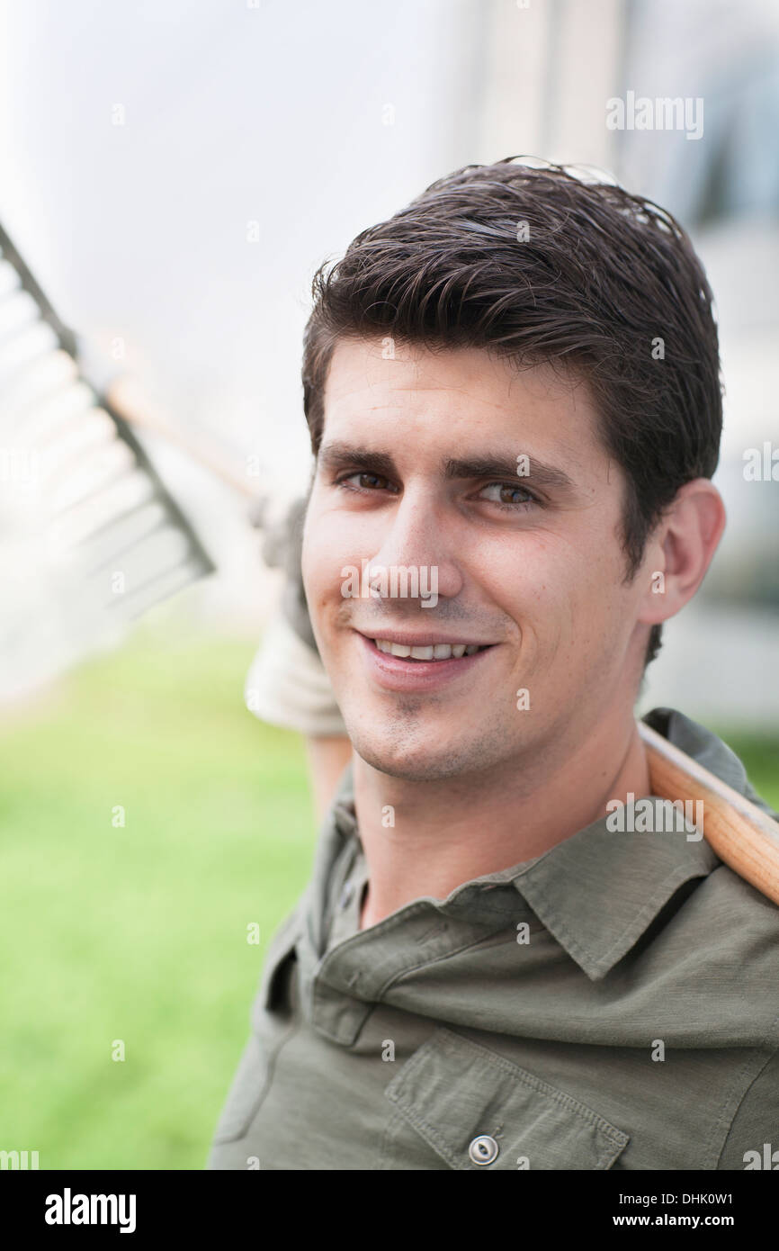 Porträt des jungen lächelnder Mann hält eine Harke auf einem Dachgarten in der Stadt Stockfoto