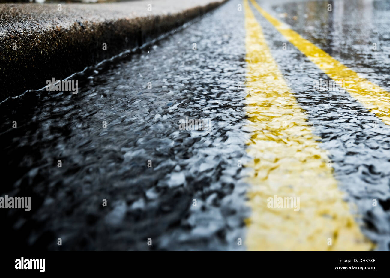 Regenwasser an der Dachrinne einer Straße mit dem Bordstein und doppelte gelbe Linien führen in die Ferne Stockfoto